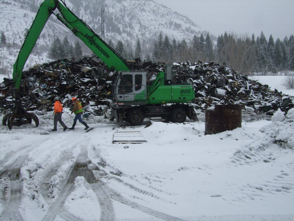 Green scrap metal machine in snowy yard.